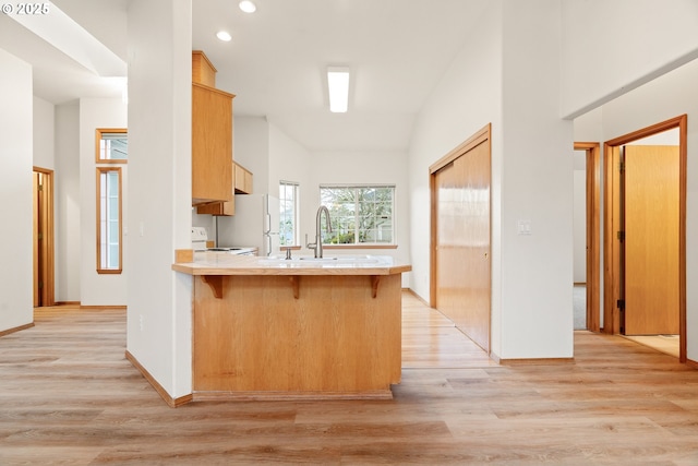 kitchen with a breakfast bar area, light countertops, light brown cabinetry, light wood-type flooring, and a peninsula