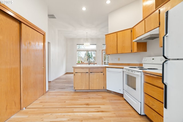 kitchen with a sink, hanging light fixtures, under cabinet range hood, light countertops, and white appliances