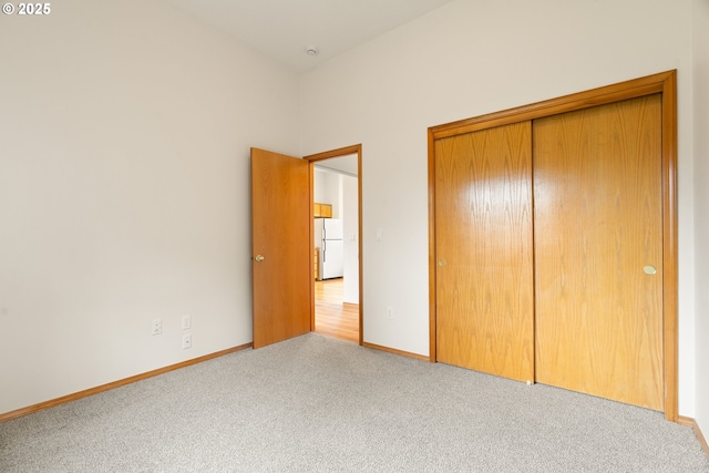 unfurnished bedroom with freestanding refrigerator, baseboards, a closet, and light carpet