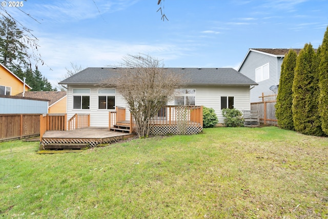 back of property with a lawn, a wooden deck, roof with shingles, and a fenced backyard