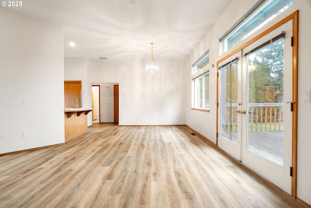 unfurnished room with light wood-type flooring, a sink, baseboards, and a notable chandelier