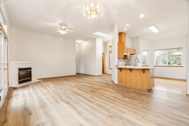 unfurnished living room featuring baseboards, a sink, a premium fireplace, light wood-type flooring, and a ceiling fan