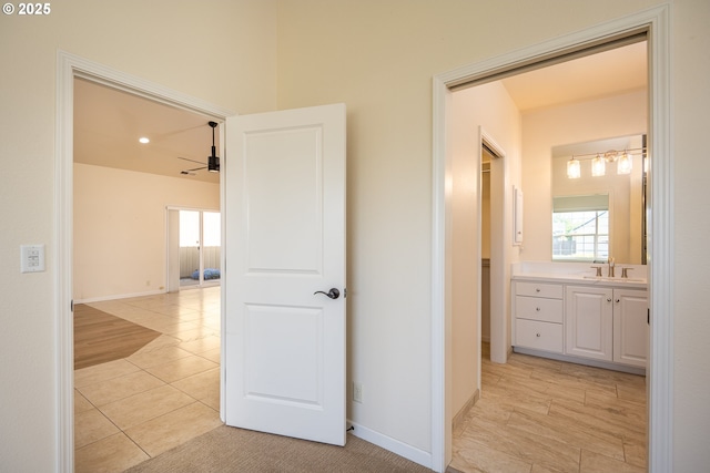 hallway featuring baseboards, a sink, light tile patterned flooring, and a healthy amount of sunlight