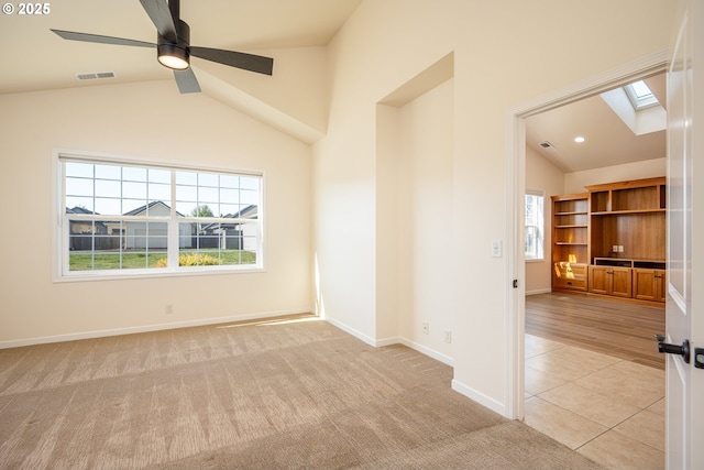 empty room featuring visible vents, a ceiling fan, vaulted ceiling with skylight, and a healthy amount of sunlight