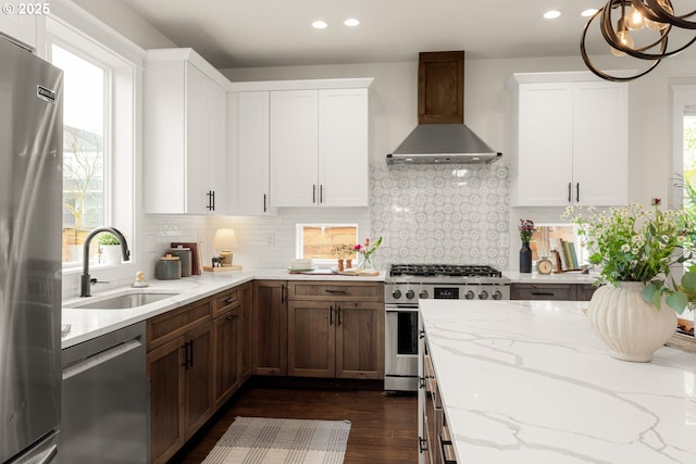 kitchen featuring dark wood-style flooring, a sink, appliances with stainless steel finishes, wall chimney exhaust hood, and backsplash