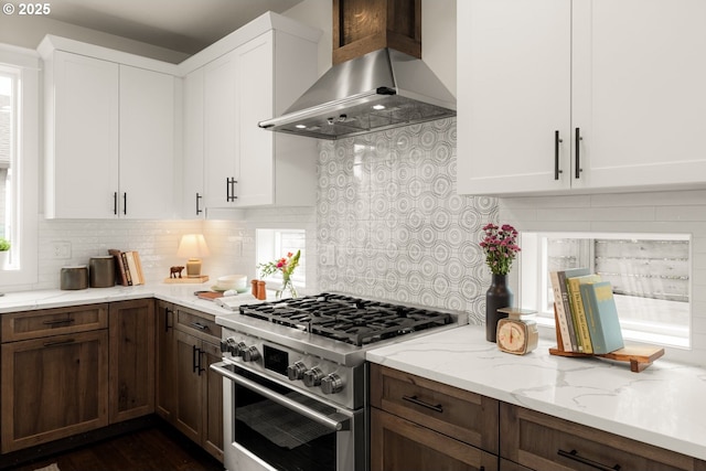 kitchen with decorative backsplash, white cabinetry, wall chimney exhaust hood, and high end stainless steel range