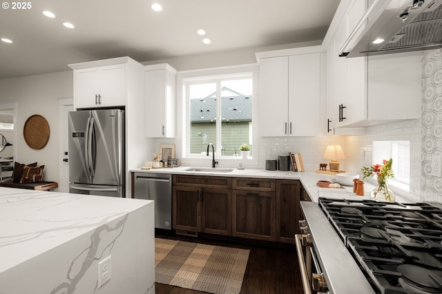 kitchen with a sink, decorative backsplash, stainless steel appliances, under cabinet range hood, and white cabinetry