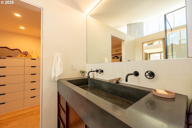 bathroom with a walk in closet, vanity, wood finished floors, and recessed lighting