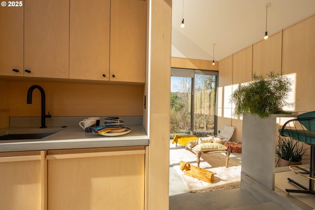 kitchen with light brown cabinets, vaulted ceiling, light countertops, and a sink