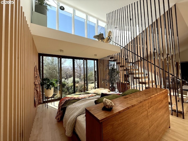 bedroom with a towering ceiling, wood finished floors, and access to exterior