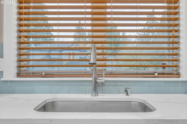 kitchen view of a sink, decorative backsplash, and light stone countertops