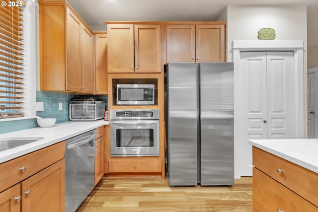 kitchen featuring appliances with stainless steel finishes, light wood finished floors, tasteful backsplash, and light stone countertops