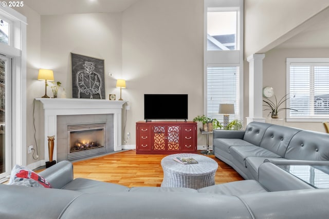 living room featuring a towering ceiling, wood finished floors, a tile fireplace, and ornate columns