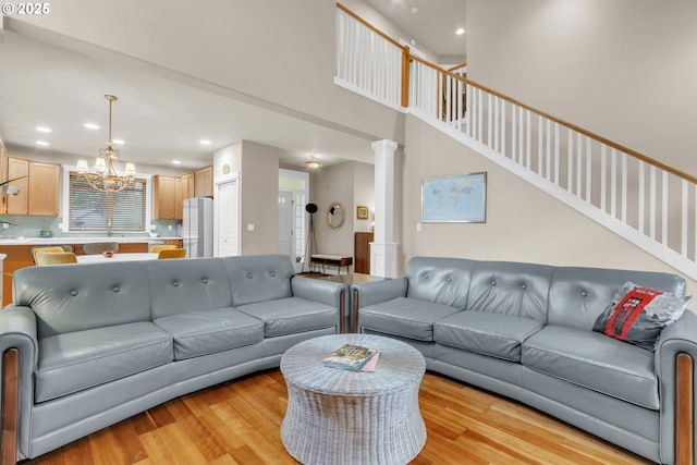 living room featuring a chandelier, light wood-style floors, recessed lighting, decorative columns, and a high ceiling