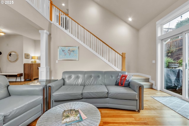 living room featuring ornate columns, light wood-style flooring, high vaulted ceiling, recessed lighting, and stairs