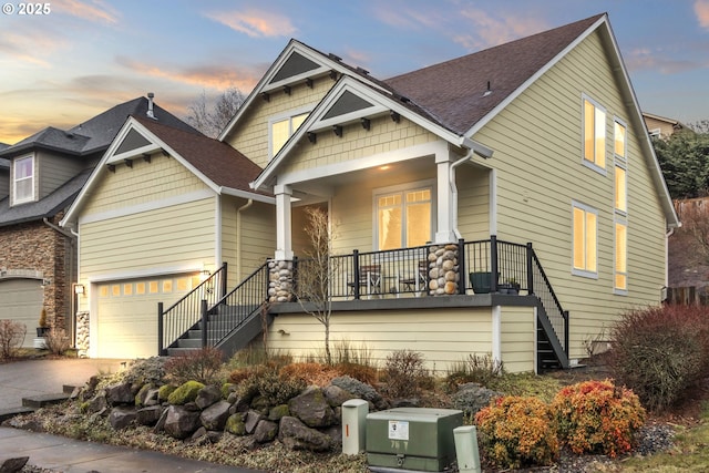 craftsman house with a porch, a garage, driveway, stairway, and roof with shingles