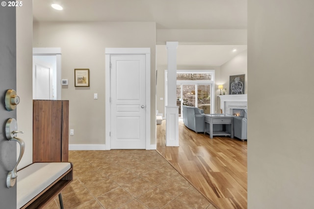 foyer entrance featuring a lit fireplace, light tile patterned floors, recessed lighting, and baseboards
