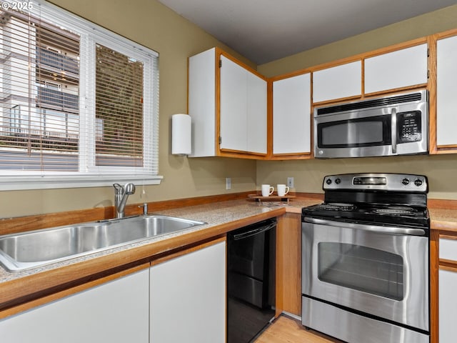 kitchen with white cabinets, light wood-type flooring, appliances with stainless steel finishes, and sink