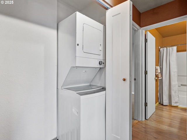 washroom with stacked washing maching and dryer and light hardwood / wood-style flooring