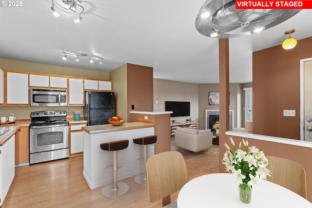 kitchen with a breakfast bar area, light hardwood / wood-style floors, stainless steel appliances, sink, and white cabinetry