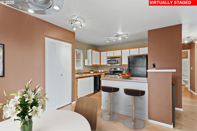 kitchen with sink, light hardwood / wood-style floors, white cabinets, and black appliances