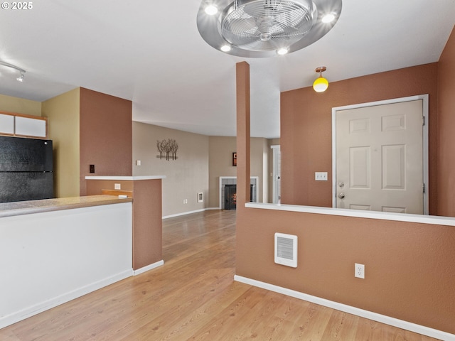 kitchen featuring light hardwood / wood-style floors, ceiling fan, black refrigerator, and a fireplace