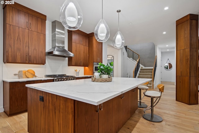 kitchen with light hardwood / wood-style floors, stainless steel appliances, hanging light fixtures, and wall chimney exhaust hood