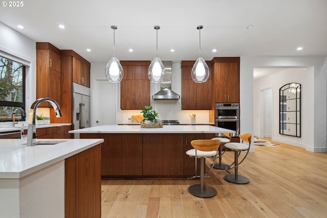 kitchen featuring pendant lighting, appliances with stainless steel finishes, wall chimney exhaust hood, light hardwood / wood-style floors, and sink