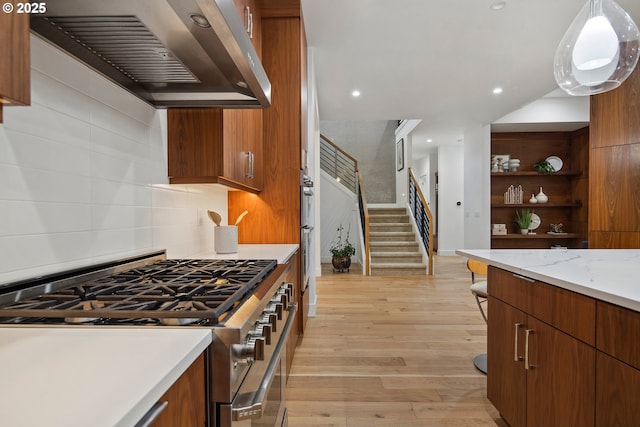 kitchen featuring appliances with stainless steel finishes, decorative light fixtures, wall chimney range hood, light stone counters, and light hardwood / wood-style flooring