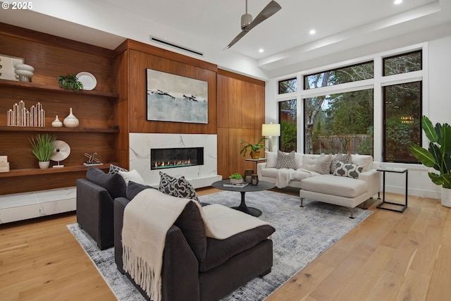 living room featuring ceiling fan, a high end fireplace, and light hardwood / wood-style flooring