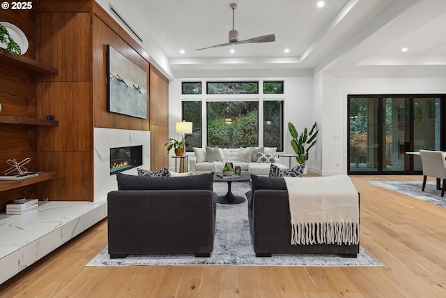 living room featuring a premium fireplace, light wood-type flooring, and ceiling fan