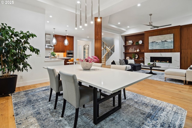 dining space with a high end fireplace, light wood-type flooring, a raised ceiling, built in features, and ceiling fan