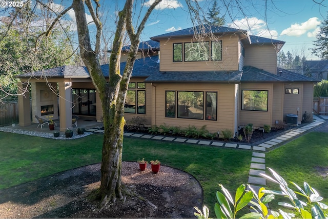 back of property featuring an outdoor fireplace, a patio, central AC, and a yard