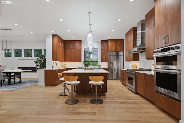 kitchen featuring pendant lighting, light hardwood / wood-style flooring, high quality appliances, a wealth of natural light, and wall chimney range hood