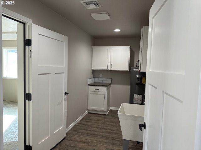 laundry area featuring visible vents, dark wood-type flooring, a sink, water heater, and baseboards