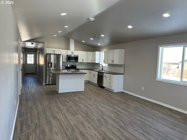 kitchen featuring dark wood-type flooring, a sink, dark countertops, appliances with stainless steel finishes, and vaulted ceiling