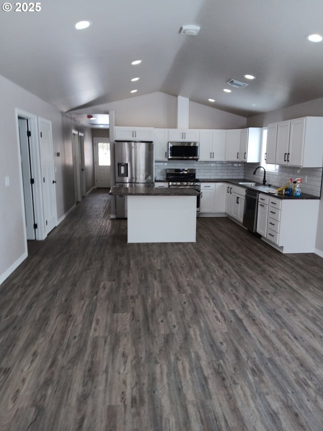 kitchen with dark countertops, tasteful backsplash, dark wood-style floors, appliances with stainless steel finishes, and lofted ceiling