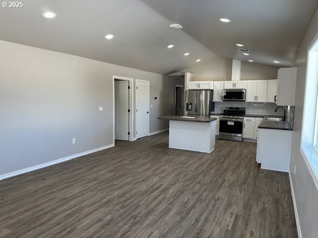 kitchen with a kitchen island, dark countertops, dark wood-style floors, open floor plan, and appliances with stainless steel finishes