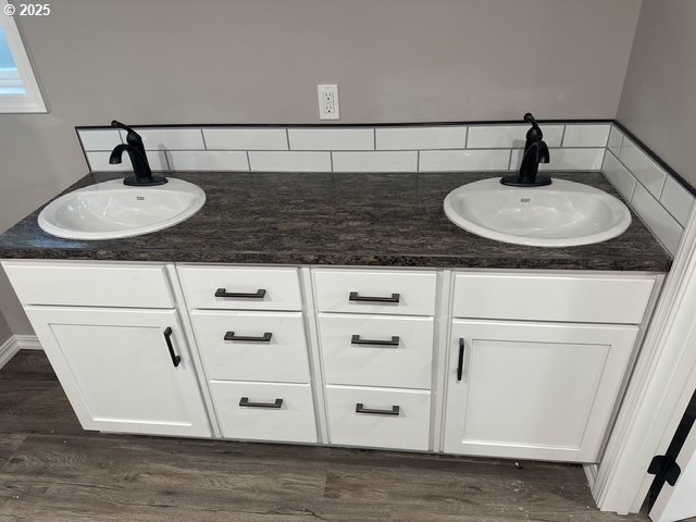 full bath with a sink, tasteful backsplash, wood finished floors, and double vanity