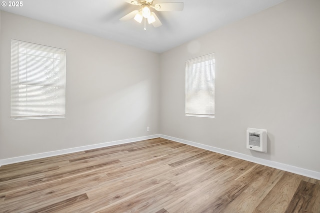 empty room featuring heating unit, a wealth of natural light, and light wood-type flooring