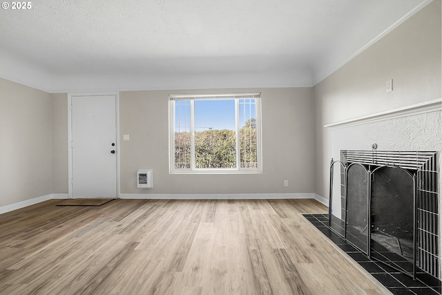 unfurnished living room with a tiled fireplace, heating unit, a textured ceiling, and light hardwood / wood-style floors