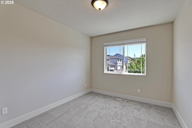 spare room featuring light colored carpet, a textured ceiling, and baseboards