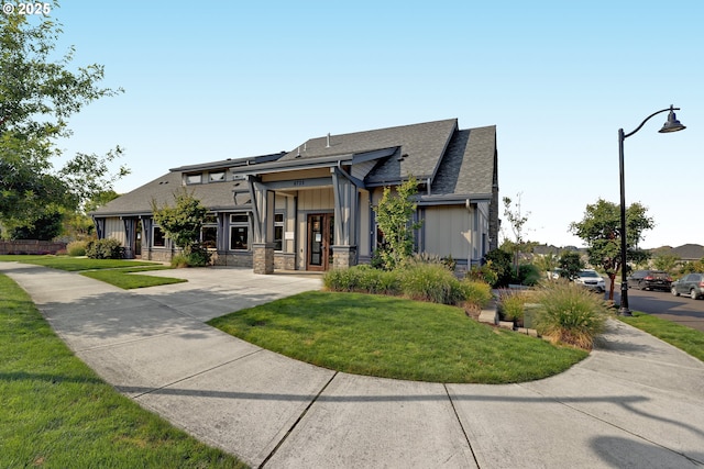 view of front facade with a front yard, board and batten siding, a shingled roof, and stone siding