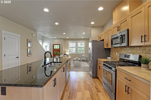 kitchen featuring stainless steel appliances, a sink, open floor plan, recessed lighting, and light wood finished floors