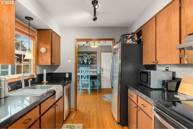kitchen with stainless steel appliances, a sink, light wood-type flooring, brown cabinetry, and pendant lighting