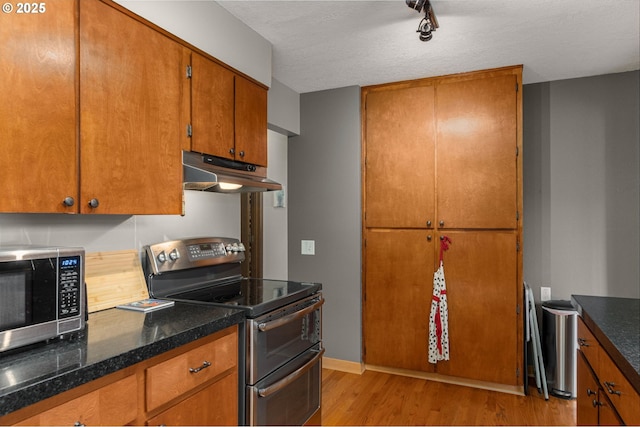 kitchen featuring under cabinet range hood, appliances with stainless steel finishes, light wood-type flooring, brown cabinetry, and baseboards