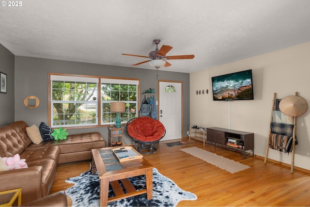 living area with a ceiling fan, wood finished floors, a textured ceiling, and baseboards
