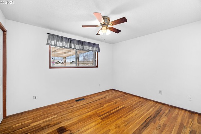 empty room featuring visible vents, a ceiling fan, and wood finished floors