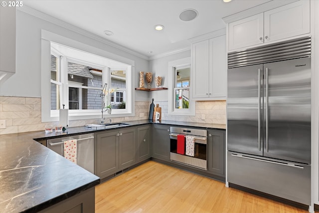 kitchen featuring stainless steel appliances, a sink, crown molding, backsplash, and light wood-type flooring