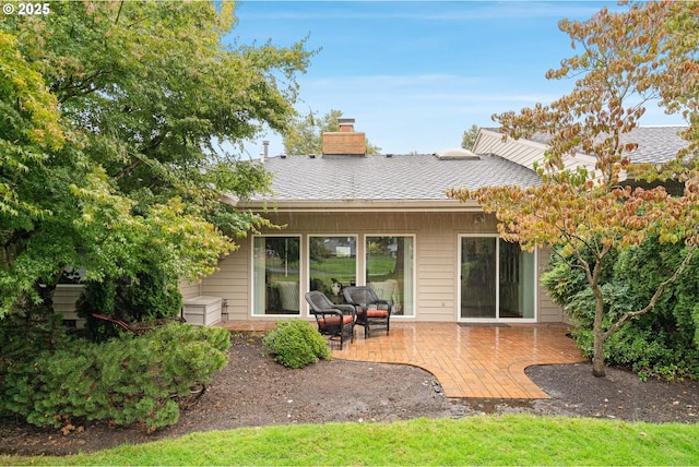 rear view of property with roof with shingles, a patio, and a chimney